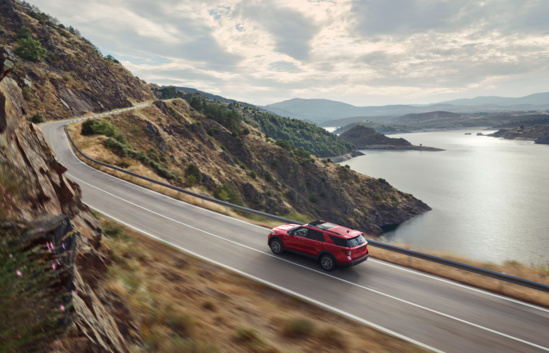 Red Ford Mustang convertible driving on scenic coastal highway with ocean and mountains in background