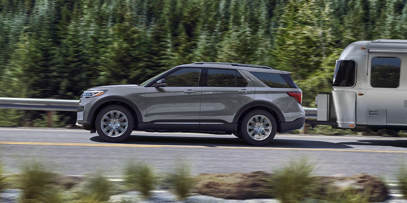 A Ford Explorer SUV driving through a highway with forest in background.
